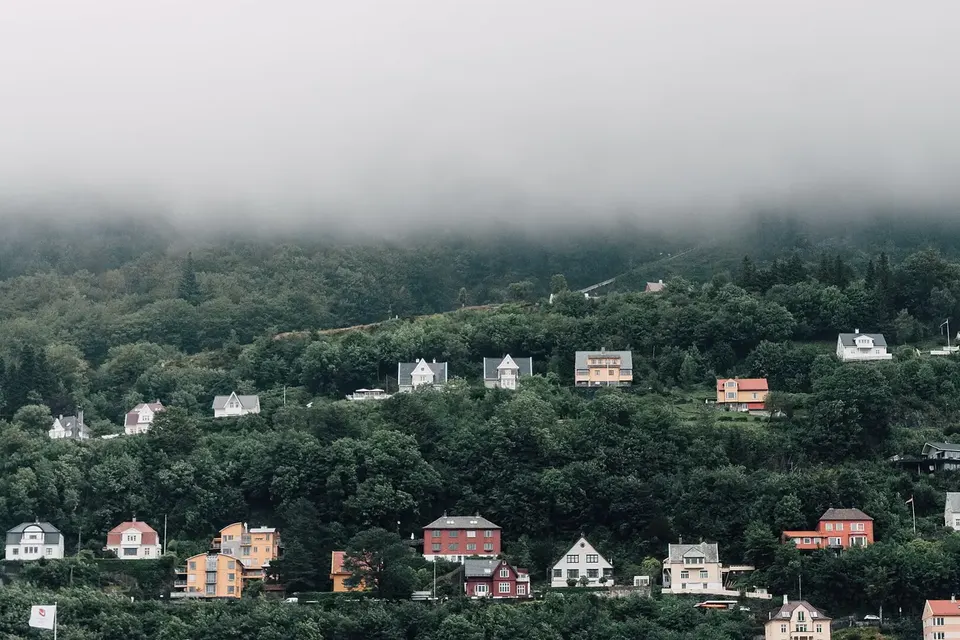 Colourful wooden houses scattered across a wooded hillside under low cloud