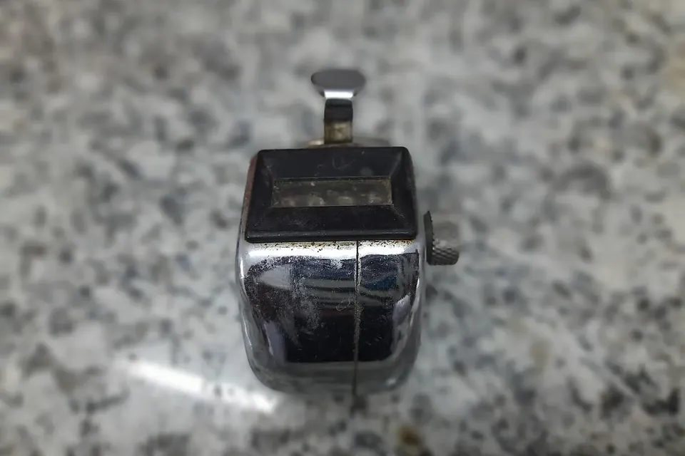 A chrome hand tally counter on a speckled granite surface