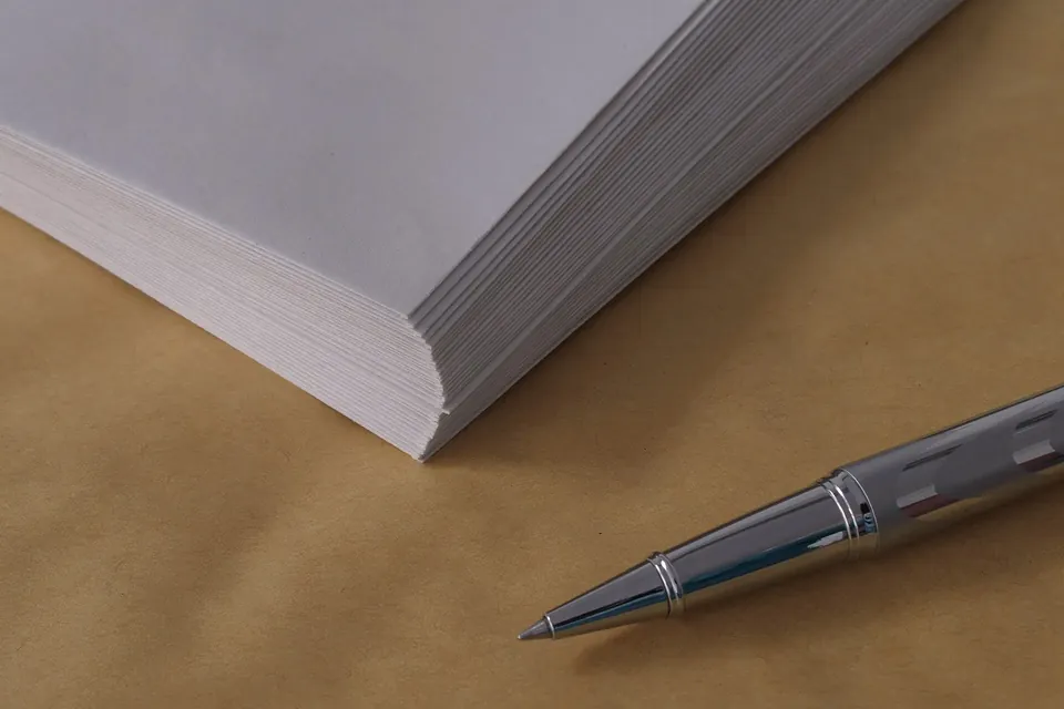 A stack of blank white envelopes and a silver pen on brown paper