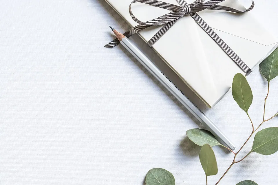White envelopes tied with a grey ribbon, a pencil and a eucalyptus sprig on a white table