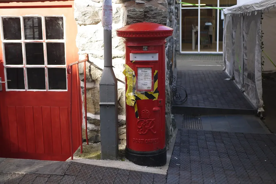A red pillar postbox beside a stone wall and a red door