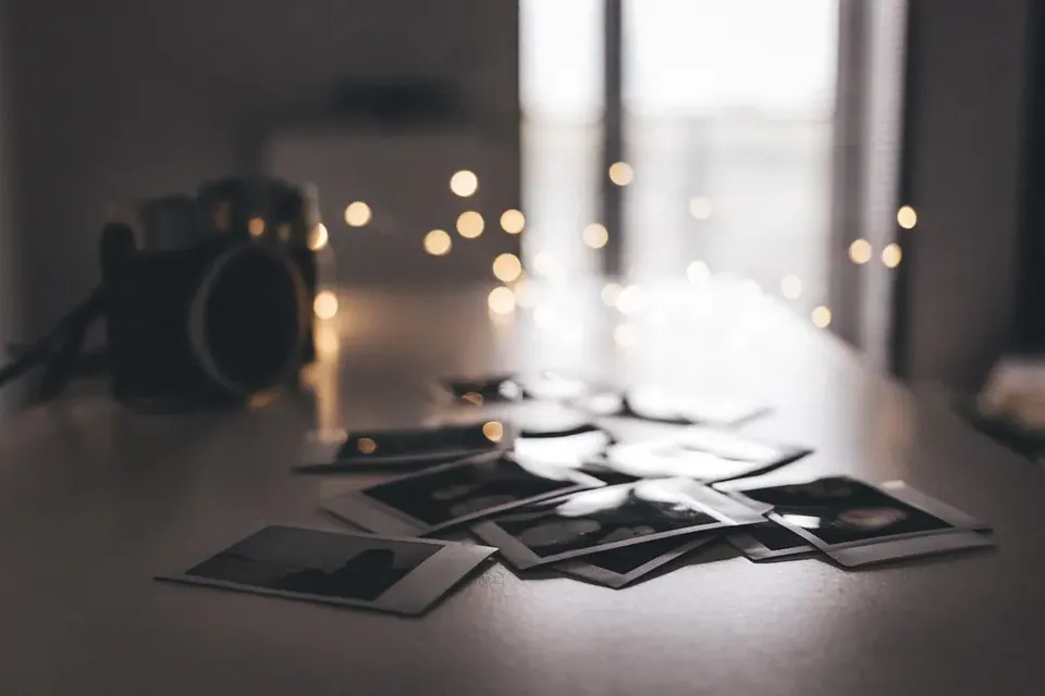 Small instant photo prints scattered on a dark table beside a camera, with lights glowing behind